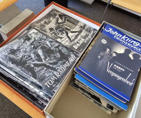 Romanhefte liegen in einem Schuhkarton auf einem Bücherwagen